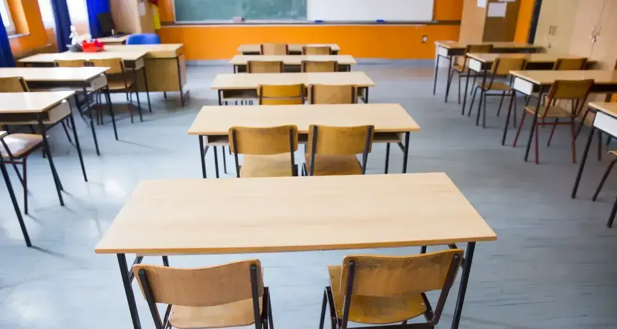 Pusta klasa szkolna z rzędami ławek i krzeseł. W tle tablica i okna. Obowiązek nauki czeka na uczniów.