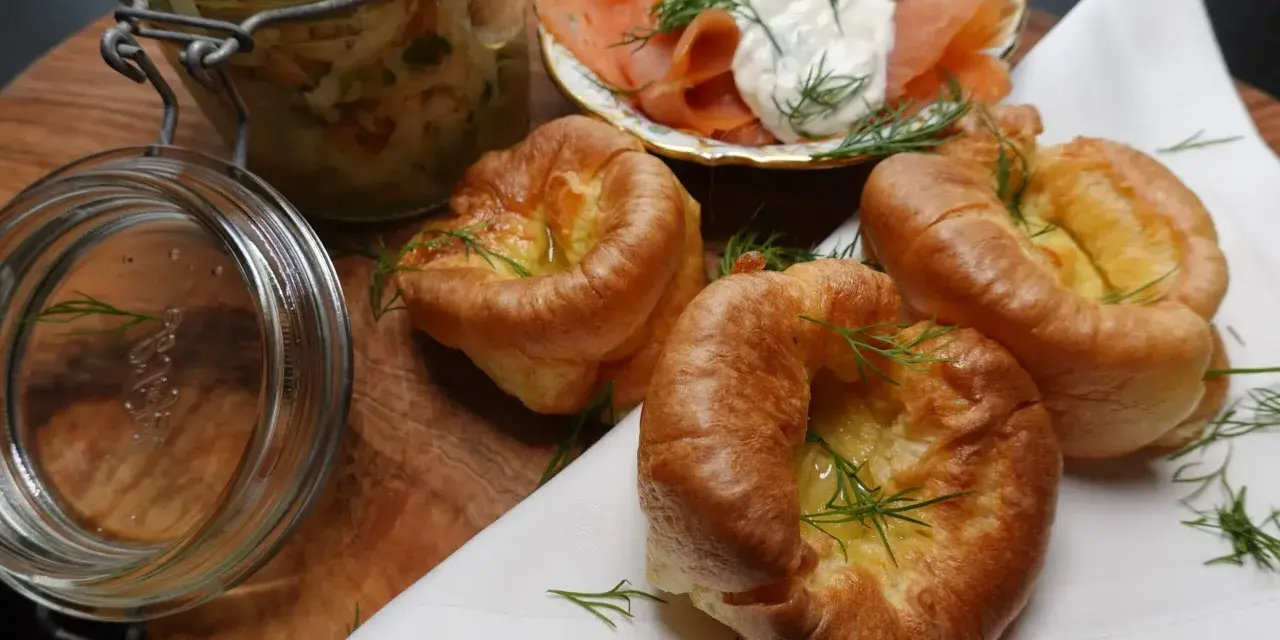 Drei goldbraune Yorkshire Pudding mit Dill garniert, daneben Lachs mit Frischkäse und ein Glas Sauerkraut.