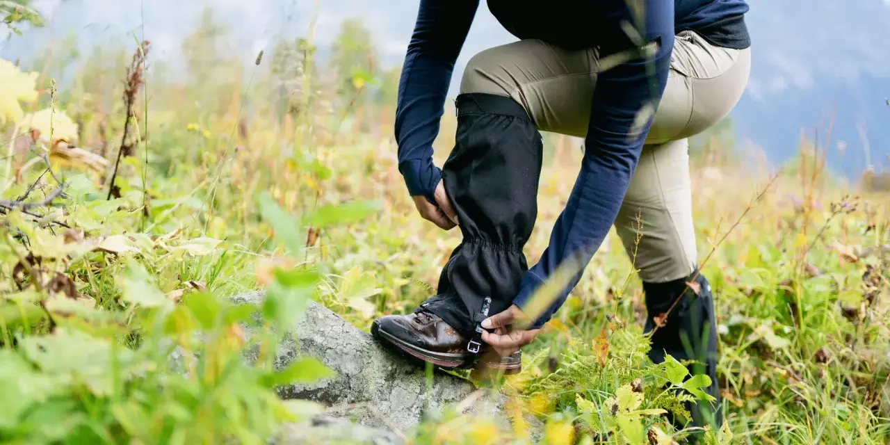 Une personne ajuste ses guetres de randonnée dans un paysage naturel.