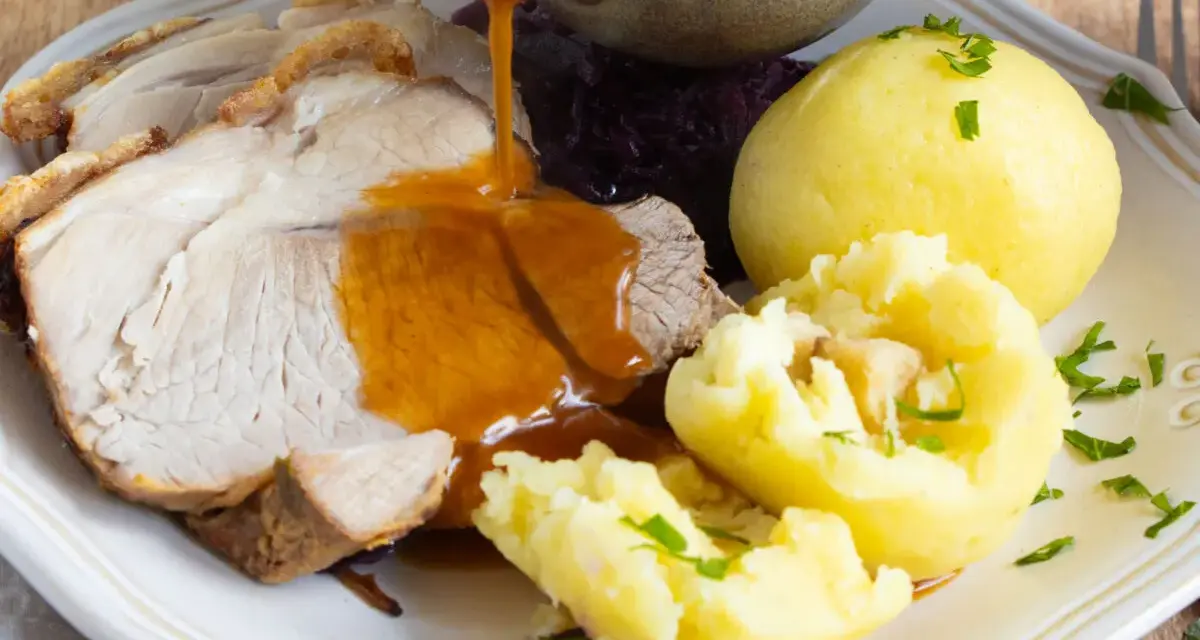 Omas Sonntagsessen: Saftiger Schweinebraten mit knuspriger Kruste, Klößen und Rotkohl, übergossen mit dunkler Soße.