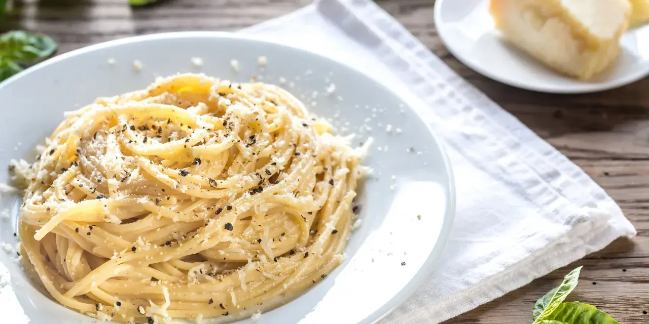 Piatto di pici cacio e pepe, conditi con abbondante pecorino e pepe nero macinato fresco, su un tavolo di legno rustico.