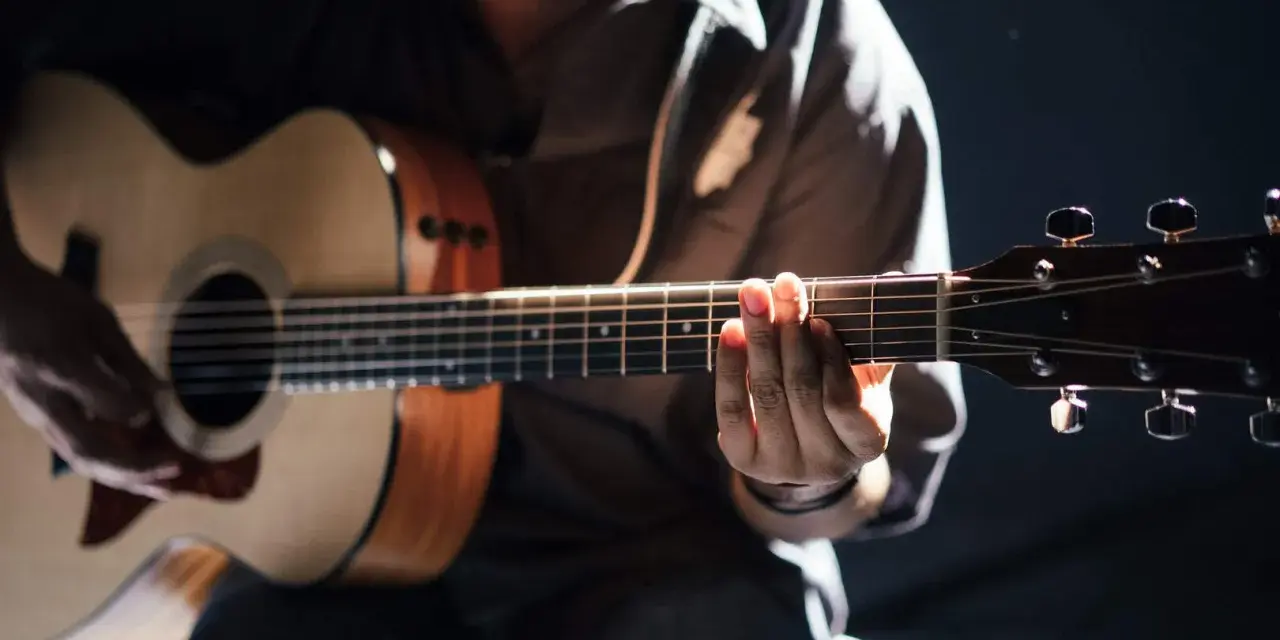 Gitarrist übt den **palm mute**-Effekt auf einer Akustikgitarre, die Finger liegen auf den Saiten.