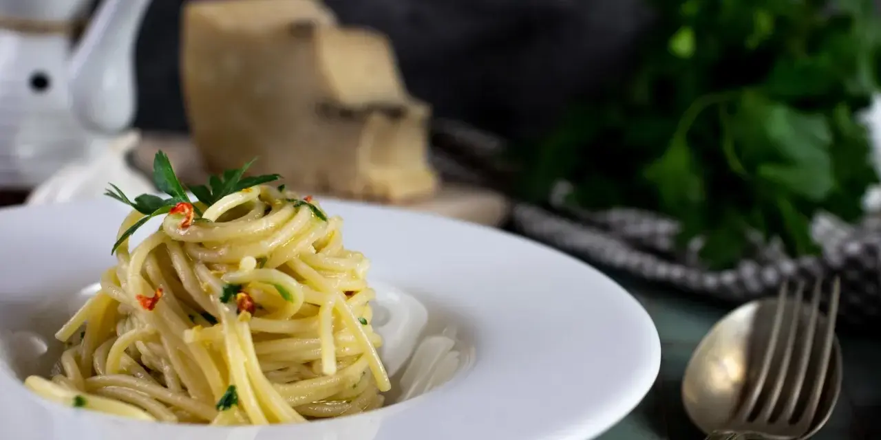 Un piatto di spaghetti alla carrettiera, conditi con aglio, olio, peperoncino e prezzemolo, con pecorino grattugiato sullo sfondo.