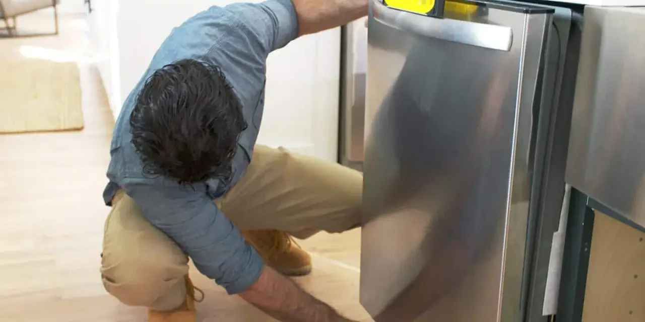 Man leveling a stainless steel dishwasher with a yellow bubble level, part of a guide on how to replace a dishwasher.
