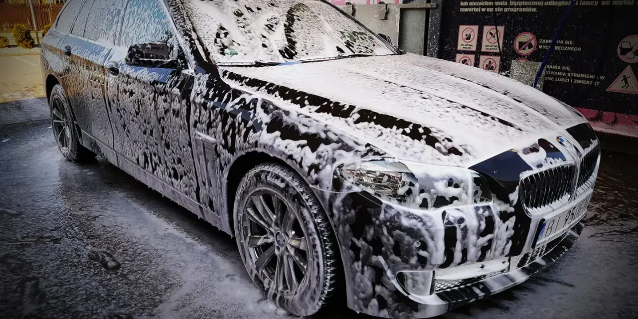 Czarny kombi pokryty pianą podczas mycia samochodu.