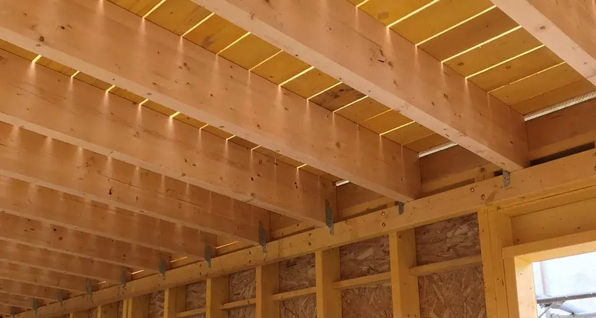 Vue détaillée de comment réaliser le solivage d'un plancher d'étage : poutres en bois, panneaux jaunes et supports métalliques.