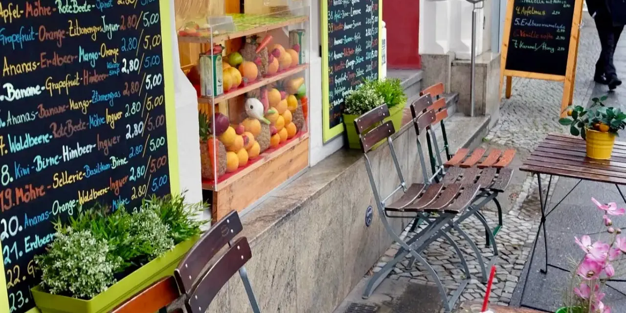 Frischer Smoothie in Berlin. Bunte Tafel mit Frucht- und Gemüsesorten, daneben leere Stühle und ein Tisch.