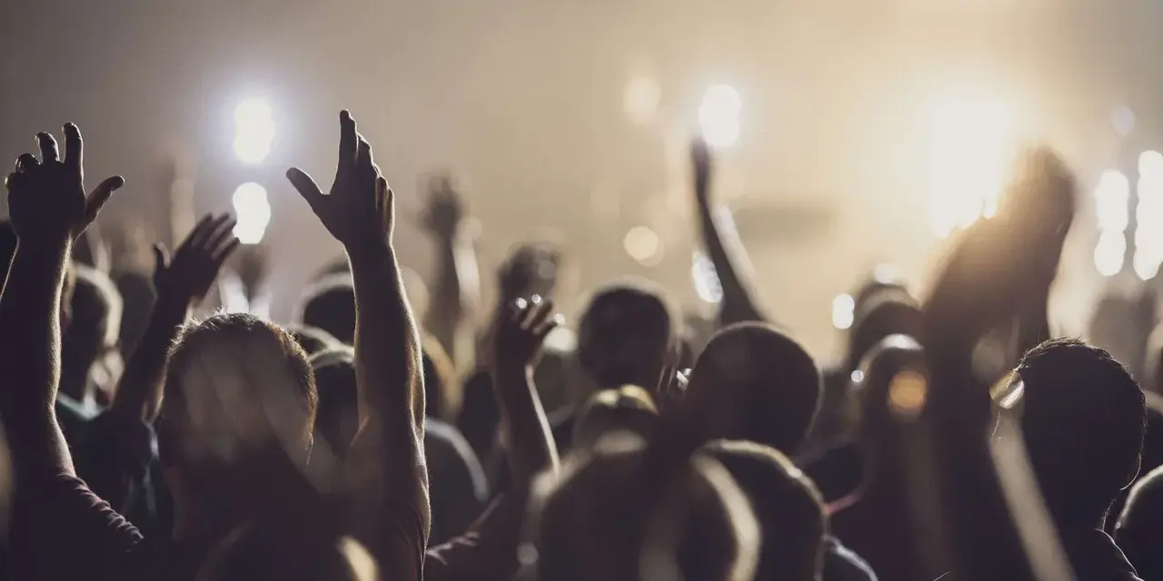 A crowd with raised hands, bathed in warm light, as if in a moment of shared worship or during powerful christian chants.