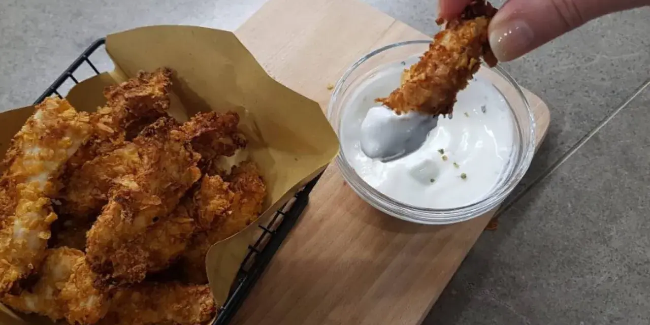 Bocconcini di pollo in friggitrice ad aria, croccanti e dorati, pronti per essere intinti in una salsa cremosa.