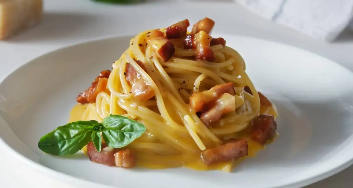 Pyszna carbonara z makaronem spaghetti, boczkiem i bazylią. W tle widać kawałek parmezanu, sugerując autentyczne carbonara skladniki.