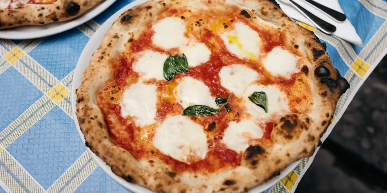 Pyszna pizza napolitana z pomidorami, mozzarellą i bazylią na niebieskim obrusie.