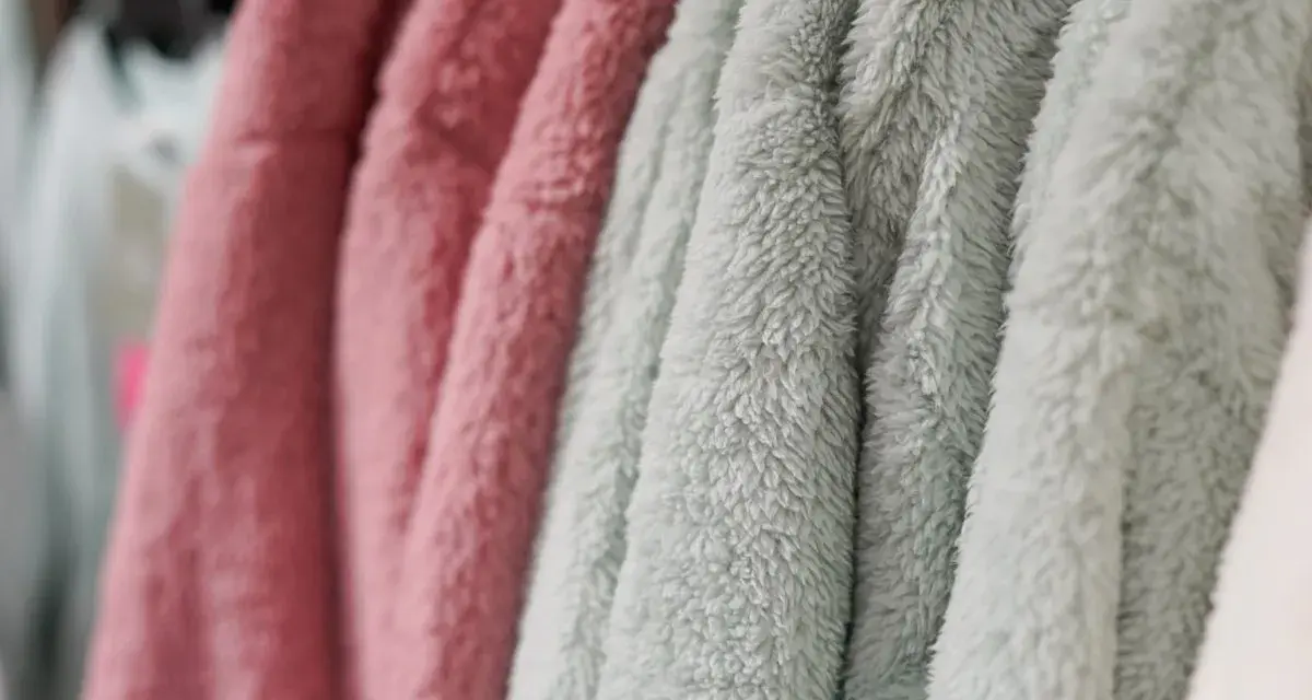 Des vêtements douillets en matière molleton, aux couleurs rose et vert d'eau, sont suspendus sur des cintres.