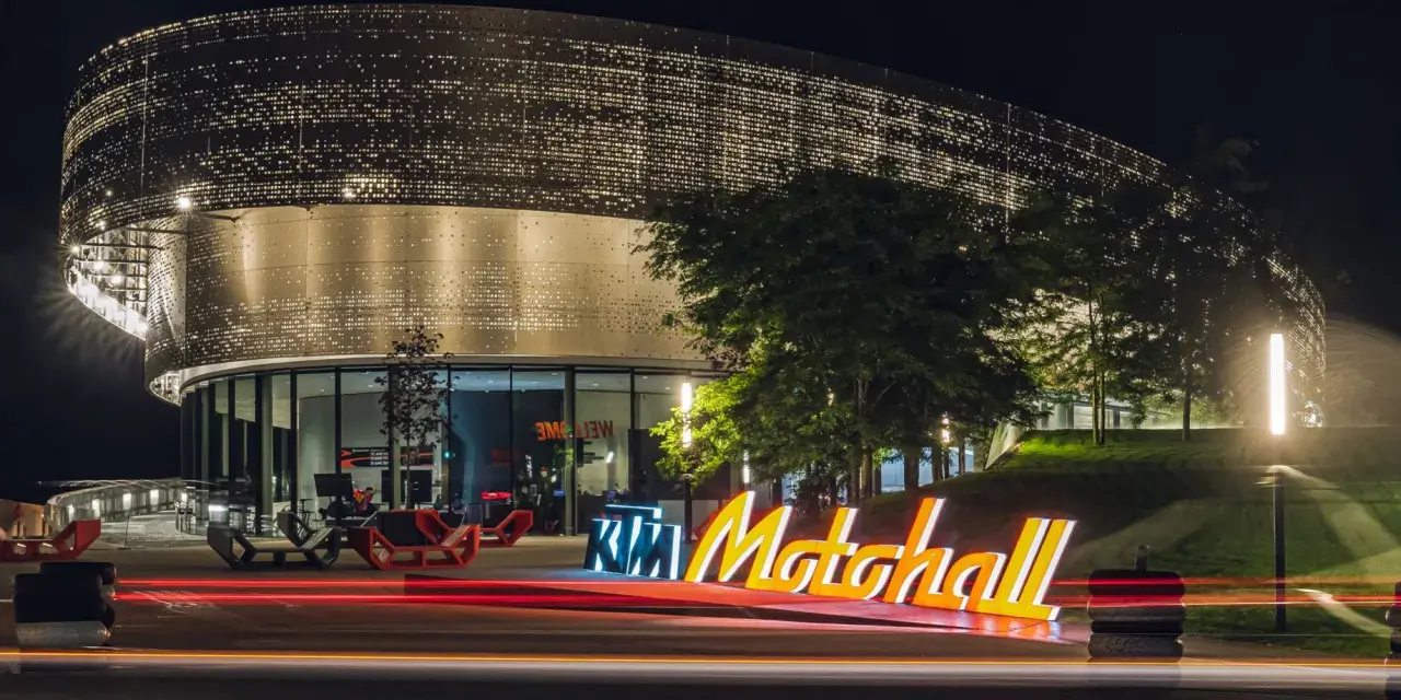 Insegna luminosa KTM Motohall di notte, con il moderno edificio illuminato e le scie luminose delle auto.
