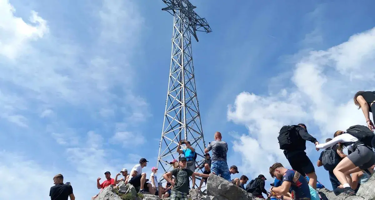 Grupa turystów na skalistym szczycie pod wieżą widokową w masywie górskim w Tatrach Zachodnich.