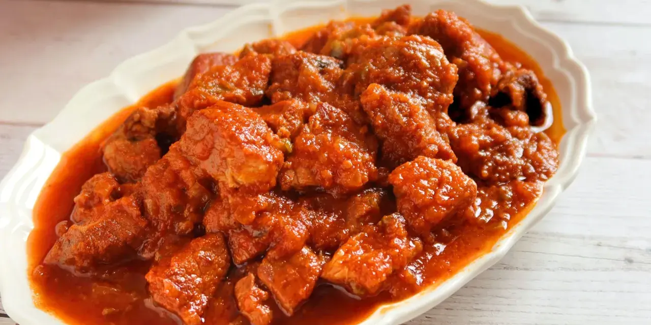 Plato de magro con tomate, trozos de carne tierna en una salsa roja y sabrosa, servido en una fuente blanca.