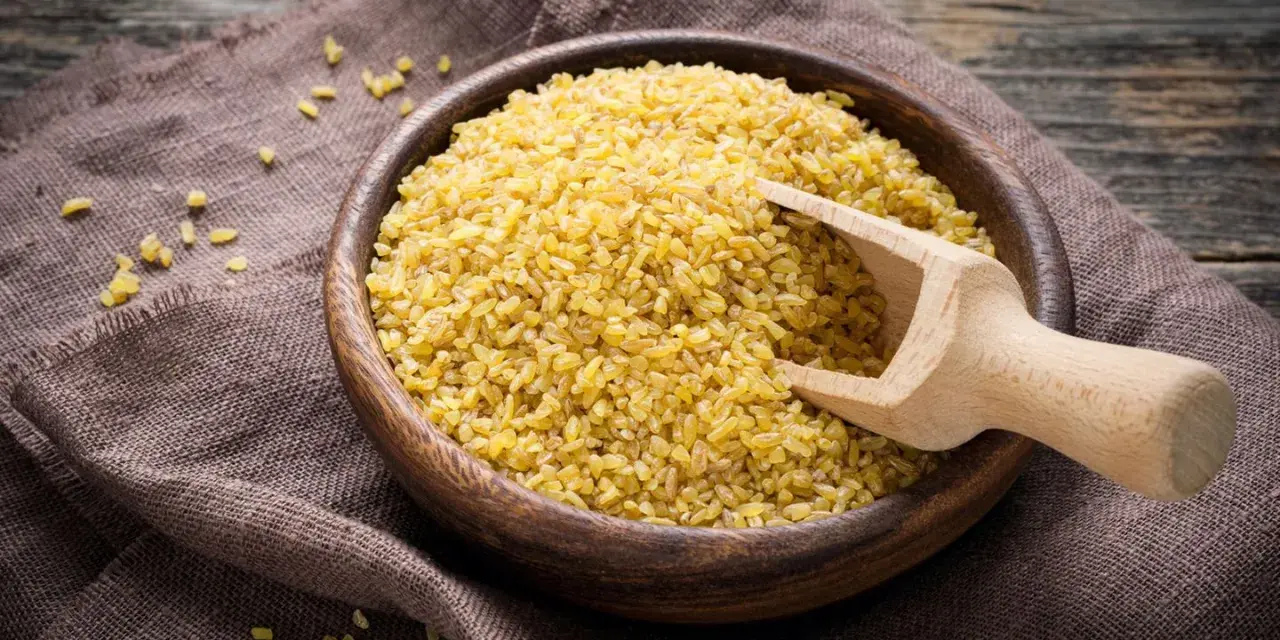 Holzschale mit Bulgur, bereit zum Bulgur kochen. Ein Holzschöpfer liegt darin.