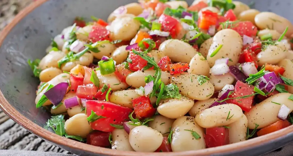 Un'insalata di fagioli sfiziosa, ricca di pomodori freschi, cipolla rossa e erbe aromatiche, servita in una ciotola rustica.