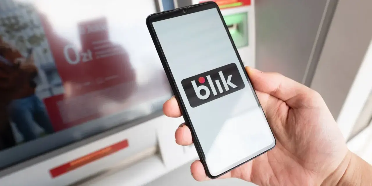 Dłoń trzyma smartfon z logo Blik. Czy Blik jest tylko w Polsce? Płatność zbliżeniowa przy bankomacie.