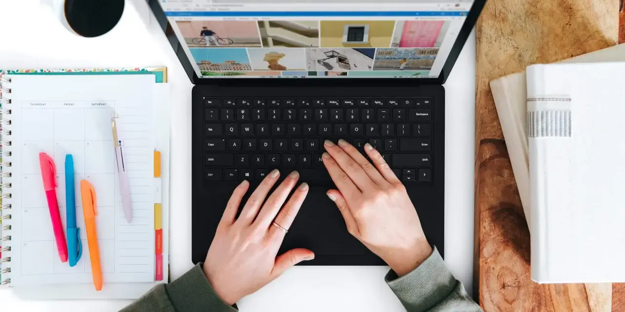Hände tippen auf einem Laptop, daneben ein Kalender und eine Kaffeetasse.