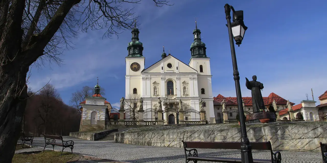 Kalwaria Zebrzydowska zwiedzanie: barokowy kościół z wieżami, kapliczki, ławki i pomnik.