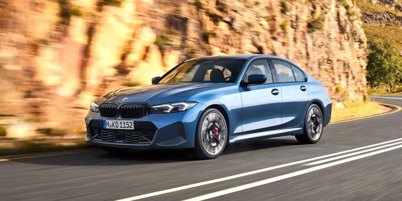 Niebieskie BMW klasy średniej jedzie po krętej drodze w skalistym krajobrazie.