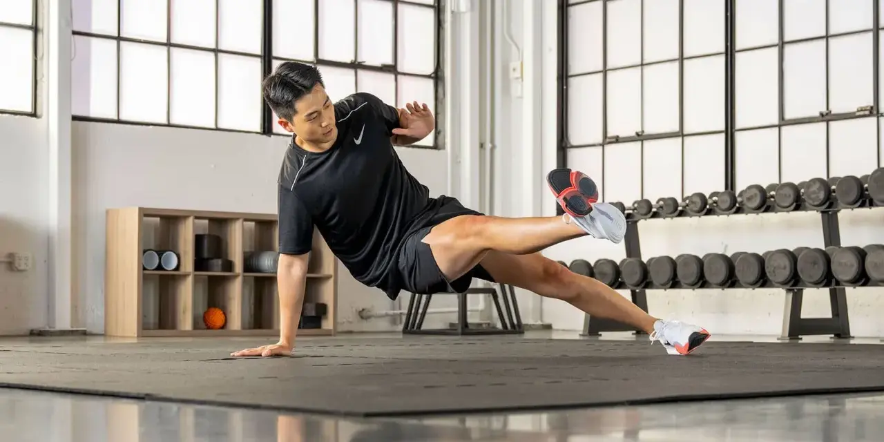 Un homme en tenue de sport exécute un exercice de planche latérale dans une salle de sport.