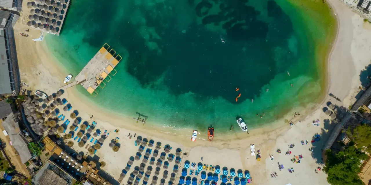 Widok z lotu ptaka na turkusowe morze i piaszczyste **albania plaże** z leżakami, parasolami i ludźmi cieszącymi się słońcem.