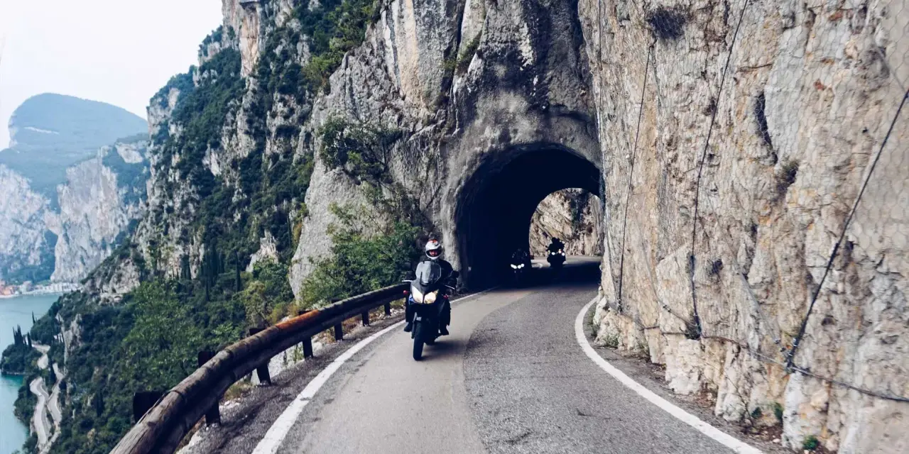 Motocykliści przemierzają malowniczą strada della forra, wjeżdżając w skalny tunel. Widok na jezioro i góry zapiera dech.