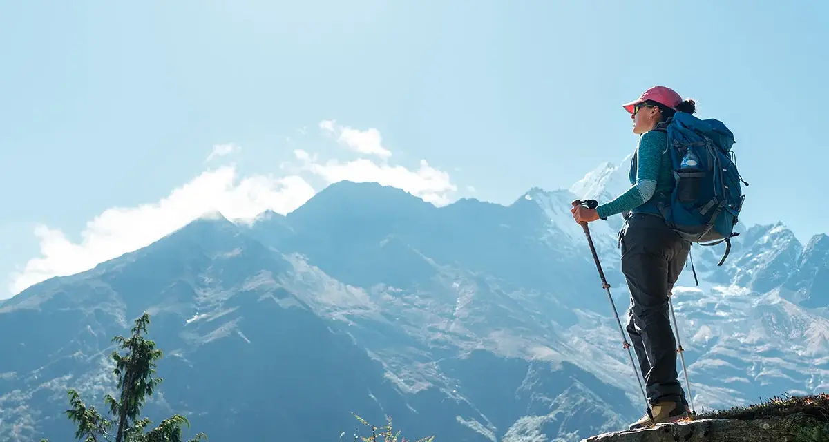 Kobieta z plecakiem i kijkami trekkingowymi podziwia majestatyczne góry podczas trekkingu pod Mount Everest.
