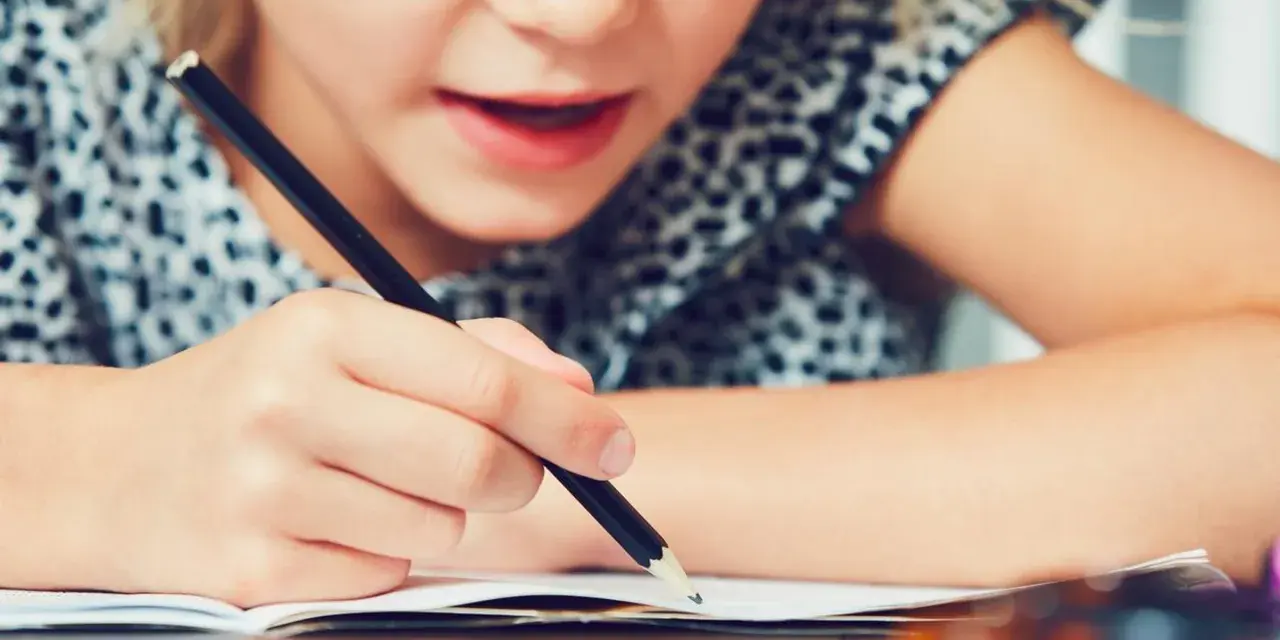 Dziecko zmagające się z pisaniem, co może być oznaką dysleksji. Skupienie na twarzy i ręce trzymającej ołówek.