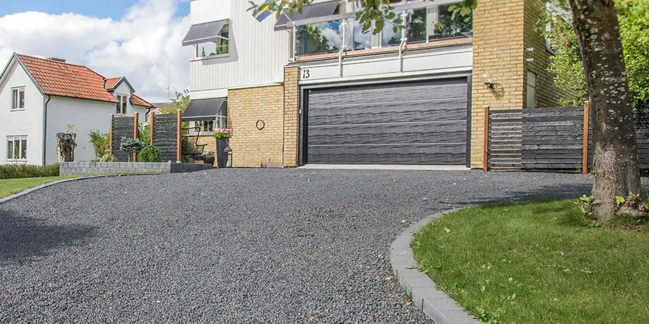 En vacker uppfart med mörkt grus leder fram till ett modernt hus med garageport.