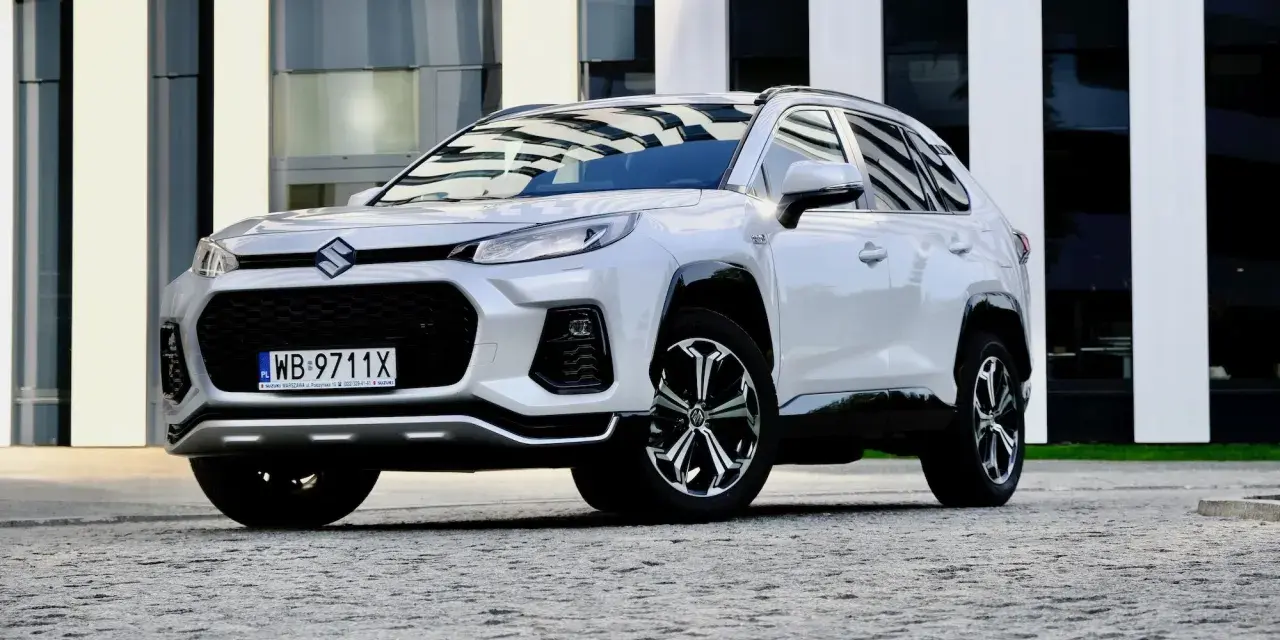 Biały Suzuki Across z czarnymi detalami stoi przed nowoczesnym budynkiem.