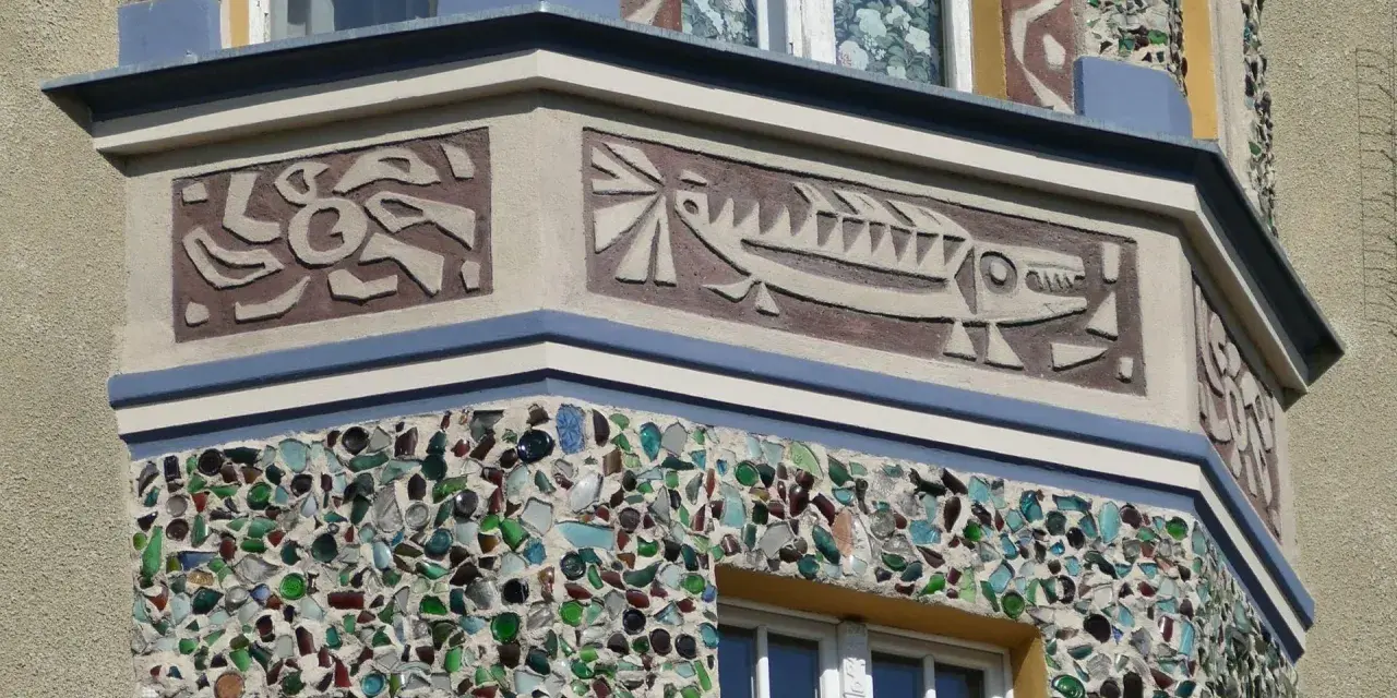 Sgraffito na fasadzie budynku: stylizowana ryba i abstrakcyjne wzory. Dolna część ozdobiona mozaiką z kolorowego szkła.