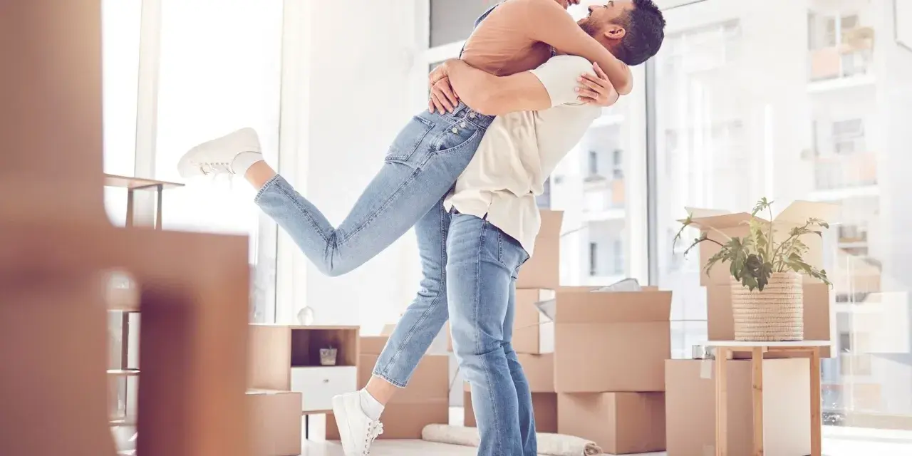 Glückliches Paar umarmt sich in einem neuen Zuhause voller Umzugskartons. Ein aufregender Moment, wann zusammenziehen!