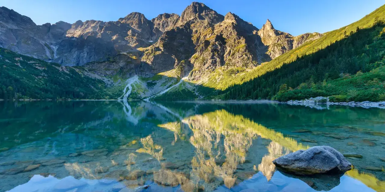 Morskie Oko jesienią. Lśniąca tafla jeziora odbija skaliste szczyty Tatr i zielone lasy.