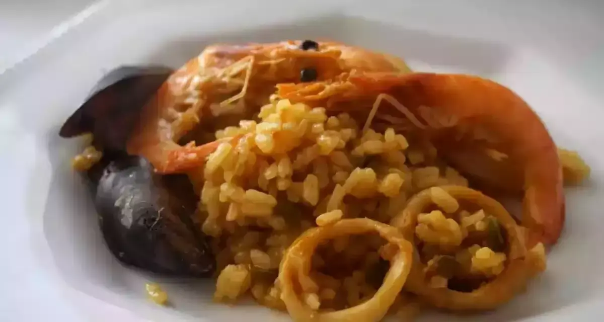 Arroz meloso con langostinos, mejillones y calamares en un plato blanco.
