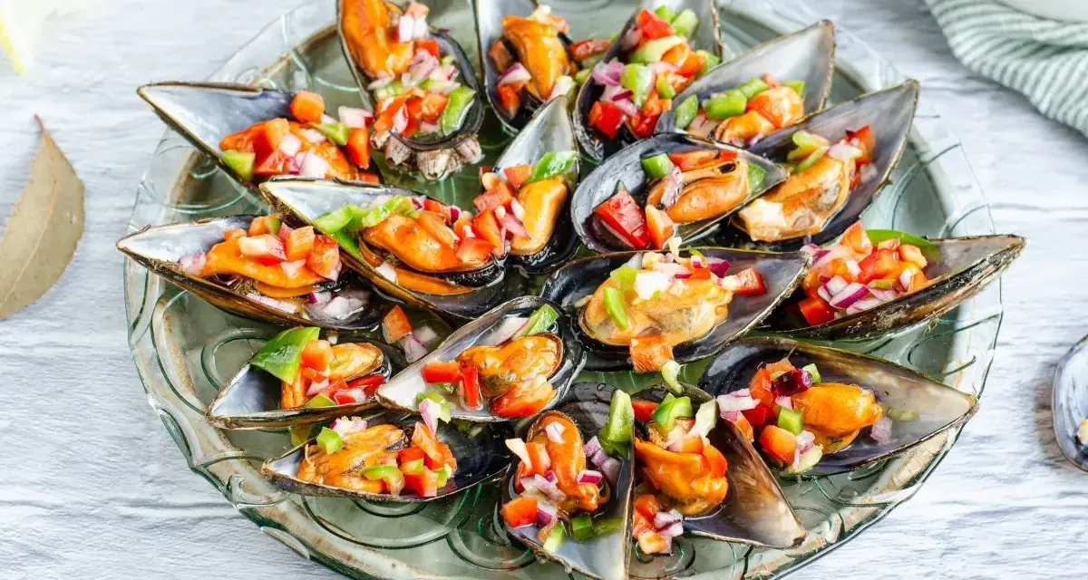 Mejillones a la vinagreta, frescos y coloridos, servidos en su concha con una picada de pimientos y cebolla.