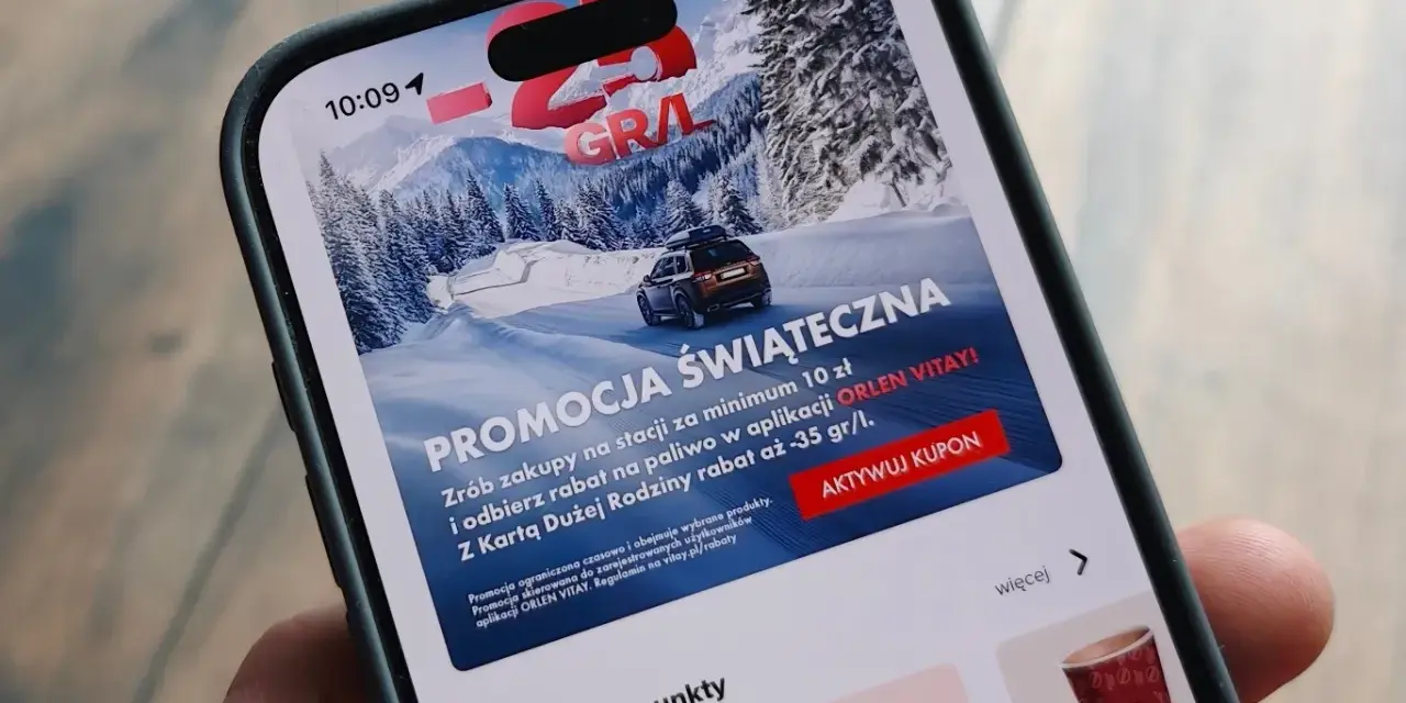 Aplikacja ORLEN z promocją na paliwo za punkty. Zima, góry i samochód na ekranie telefonu.