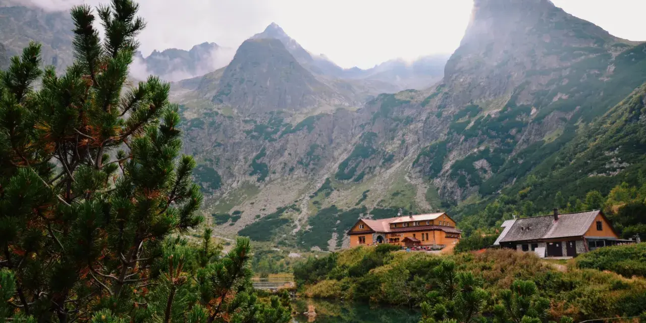 Malownicze tatry słowackie z górami w chmurach, jeziorem i schroniskami.