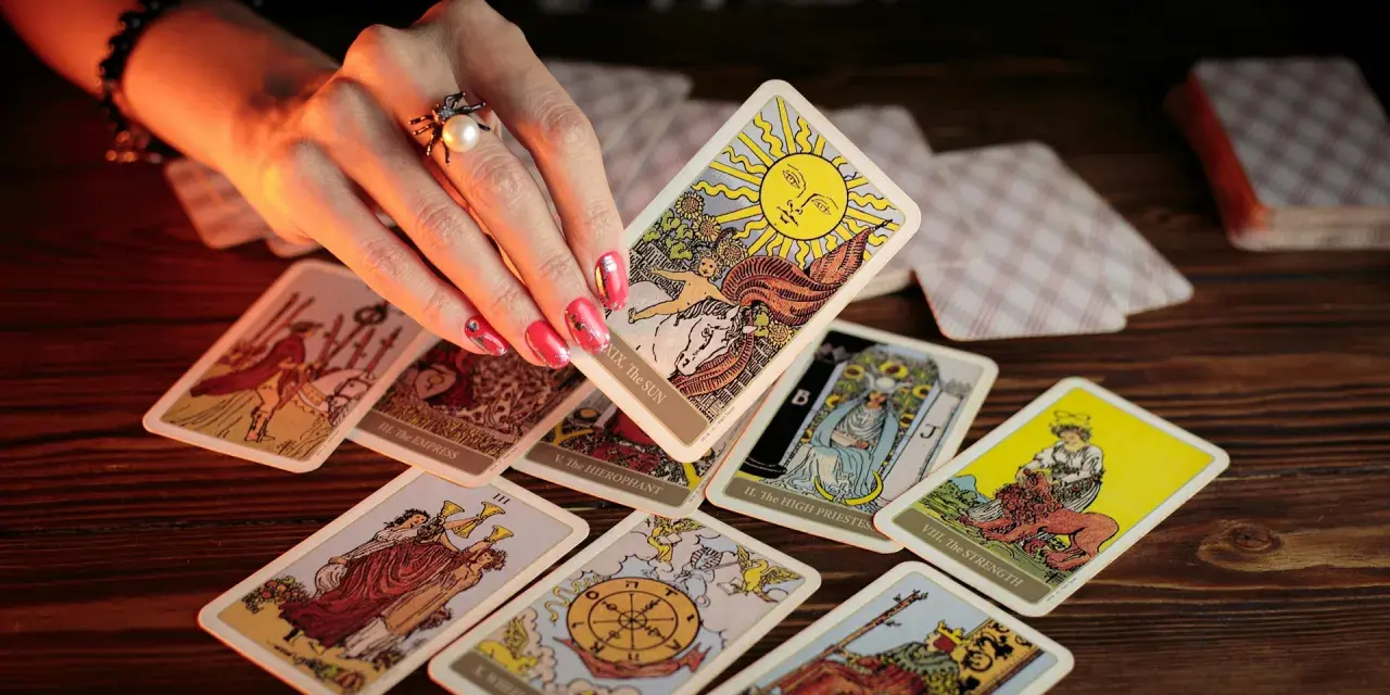 Dłoń z pierścionkiem wybiera kartę Słońce z talii tarot. Rozłożony krzyż celtycki tarot zapowiada przyszłość.