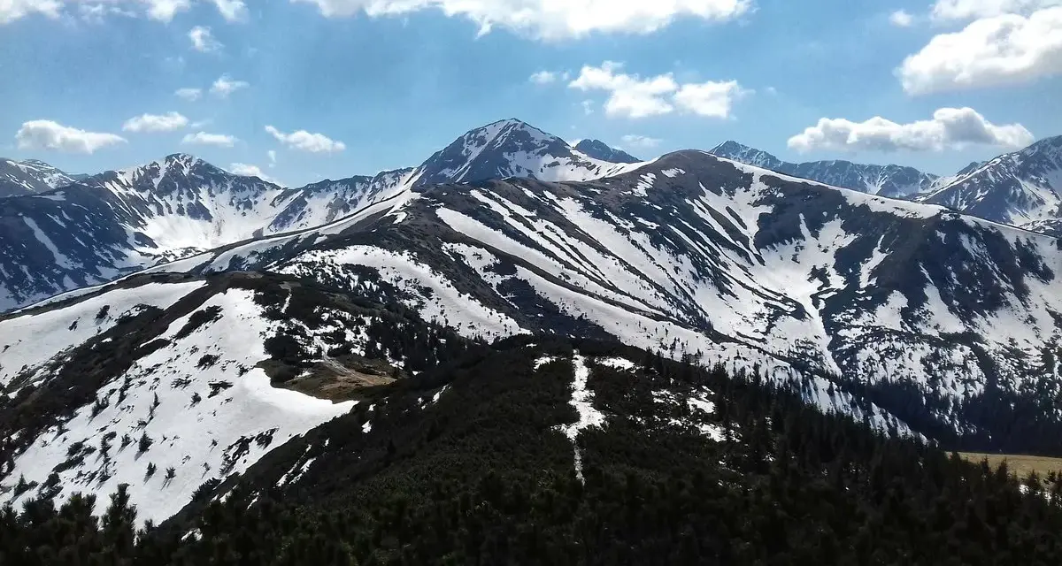 Majestatyczne Tatry w kwietniu, pokryte śniegiem szczyty i zielone lasy.