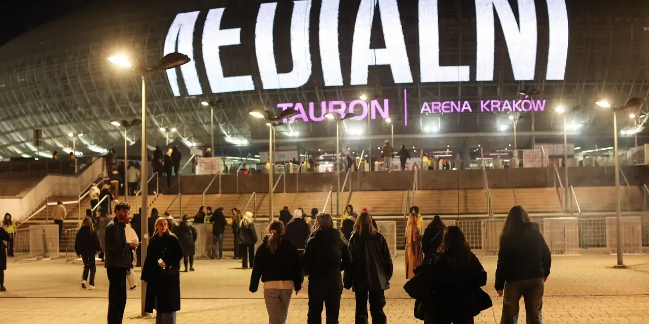 Tłum ludzi zmierza do Tauron Areny Kraków na koncert. Wielki napis na dachu obiektu zapowiada wydarzenie. To prawdziwy **rush w Polsce**!