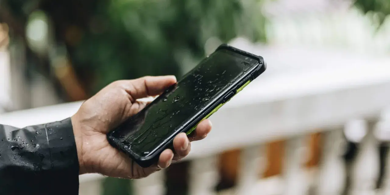 Dłoń trzyma mokry smartfon. IPX4 co oznacza? Ochronę przed zachlapaniem, idealny na deszcz.