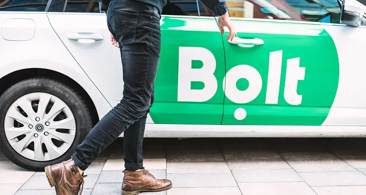 Chcesz wiedzieć, jak zostać kierowcą Bolta? Mężczyzna otwiera drzwi białego samochodu z zielonym logo Bolt.