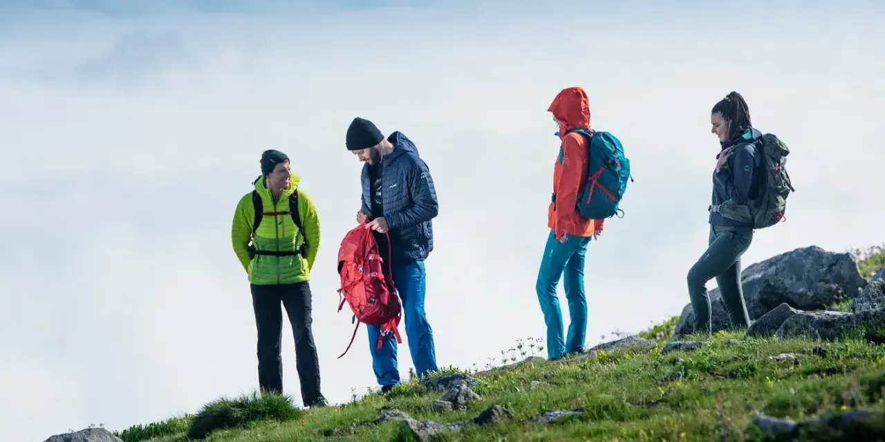 Cztery osoby w górskim krajobrazie, przygotowujące się do wyprawy. To właśnie jest co to trekking – przygoda i odkrywanie natury.