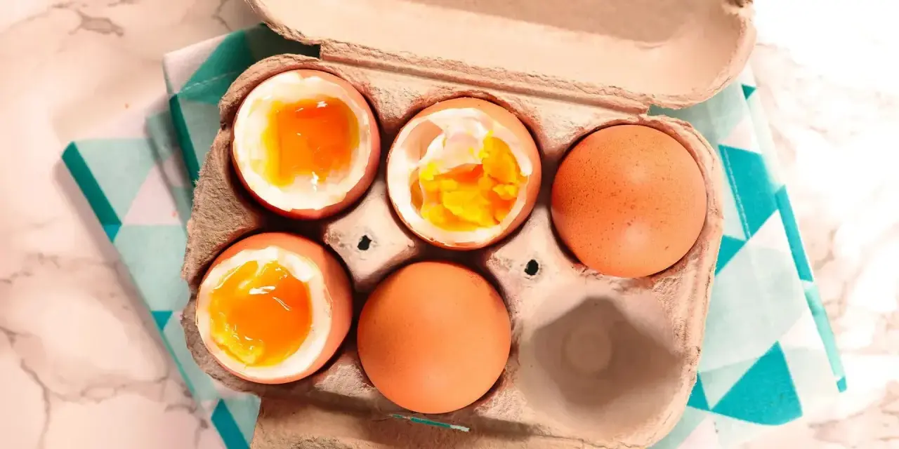 Uova alla coque in un cartone, alcune aperte mostrano tuorli dorati e cremosi, pronte per essere gustate.