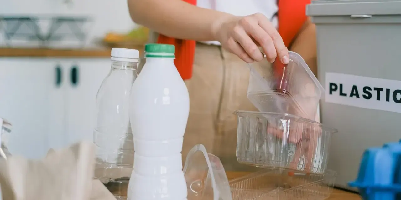 Segregacja odpadów to pierwszy krok, jak ograniczyć plastik. Ręka wrzuca plastikowe opakowania do pojemnika z napisem "PLASTIC".