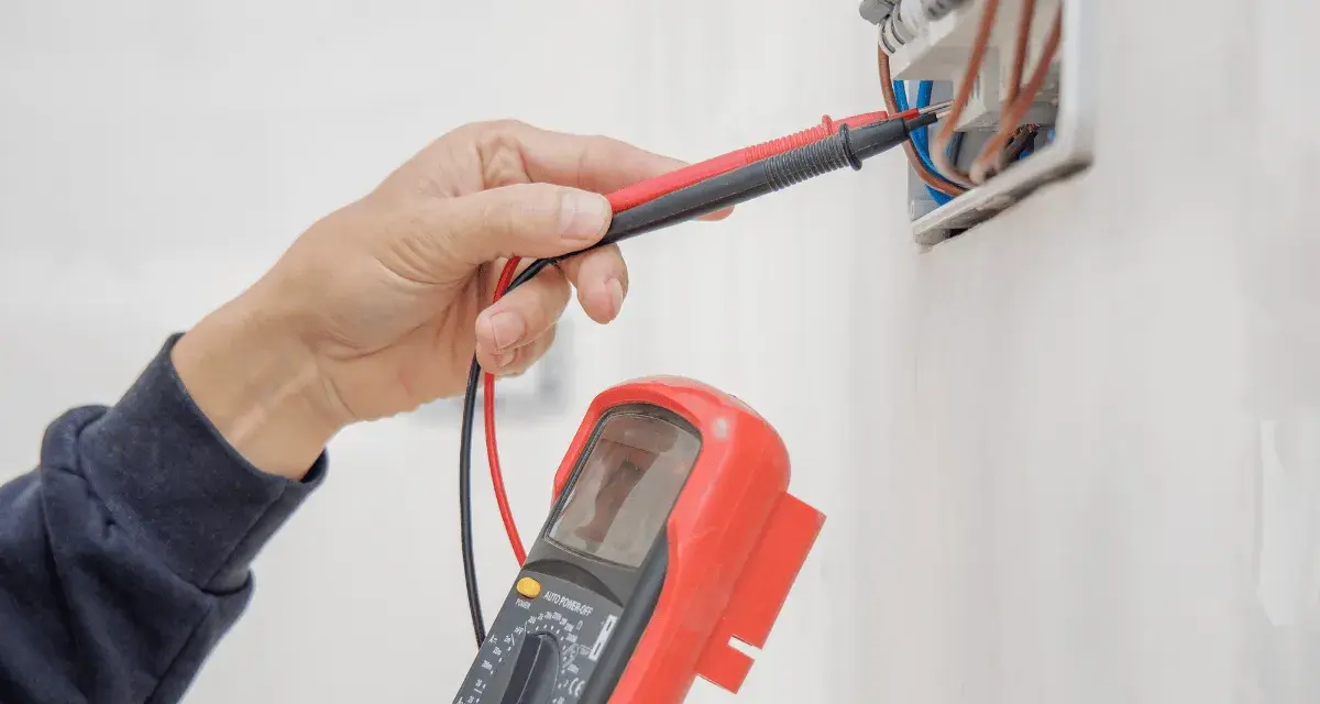 Elektryk sprawdza instalację elektryczną multimetrem, przygotowując protokół odbioru.