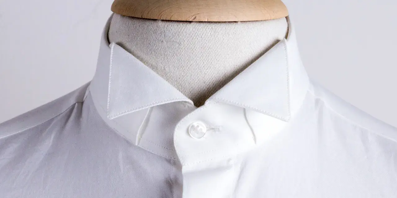 Dettaglio di una camicia bianca su un manichino, che mostra i diversi tipi di colletto camicia.