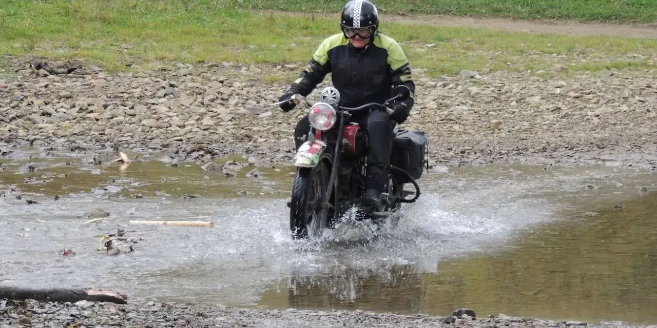 Motocyklista w kasku pokonuje wodną przeszkodę na kamienistej trasie w okolicach Jasła.